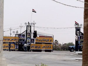 Agents du Vevak et soldat irakien devant les panneaux de propagande et les haut-parleurs installés sur le portail de l'entrée principale d'Achraf